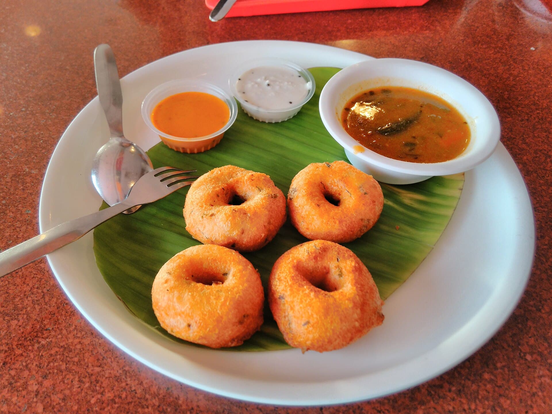Medu vada with sambar and chutneys on a banana leaf